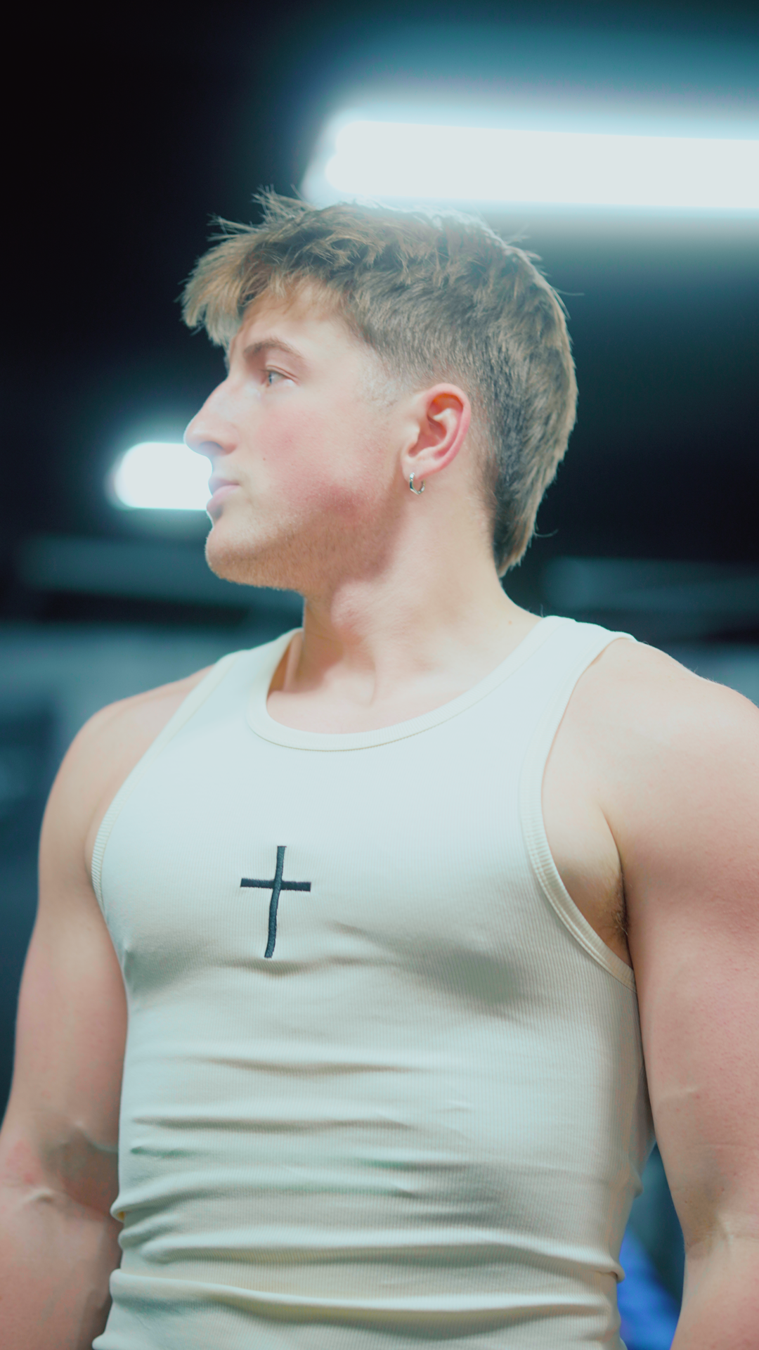 Saint Kaizen Cross Stringer - Cream. Christian gym wear tank top with a bold cross symbol design. Deep-cut, performance fit for maximum range of motion during lifts.
