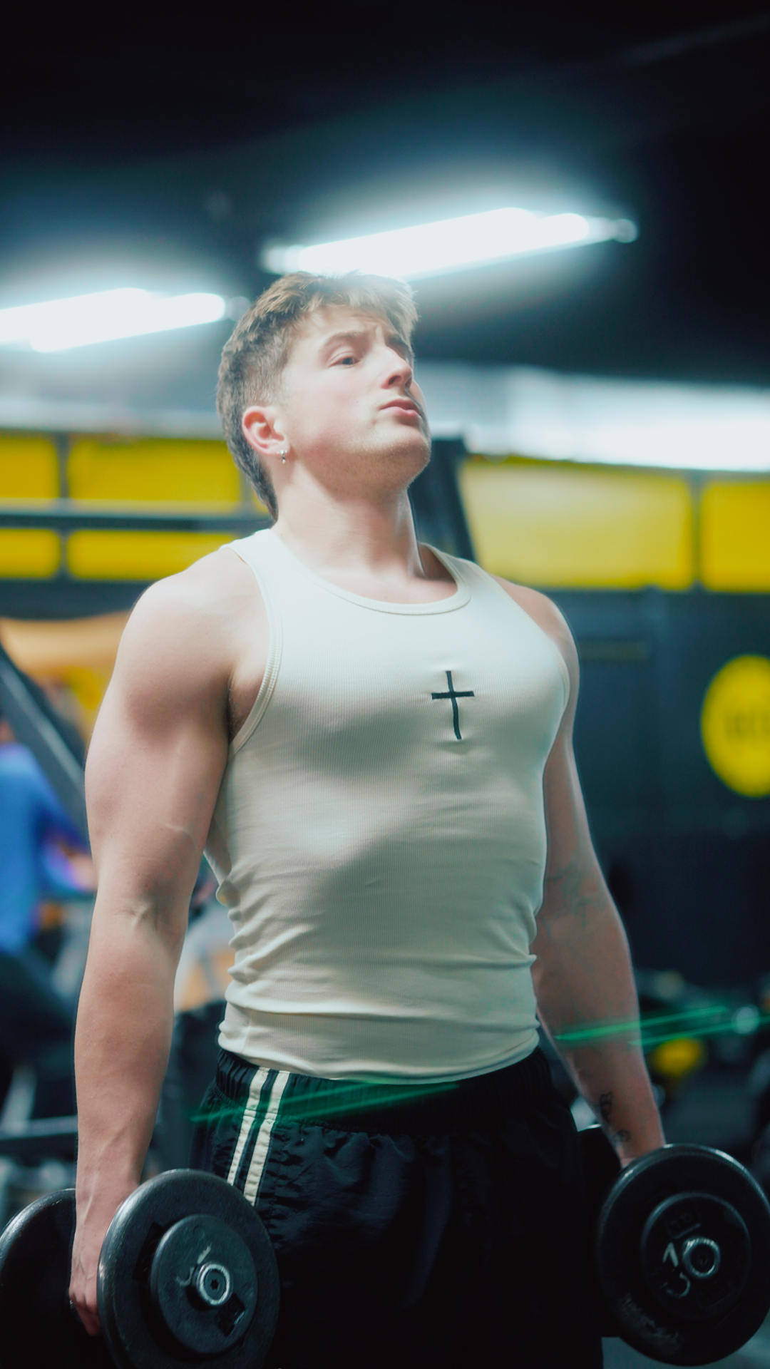 Saint Kaizen Cross Stringer - Cream. Christian gym wear tank top with a bold cross symbol design. Deep-cut, performance fit for maximum range of motion during lifts.