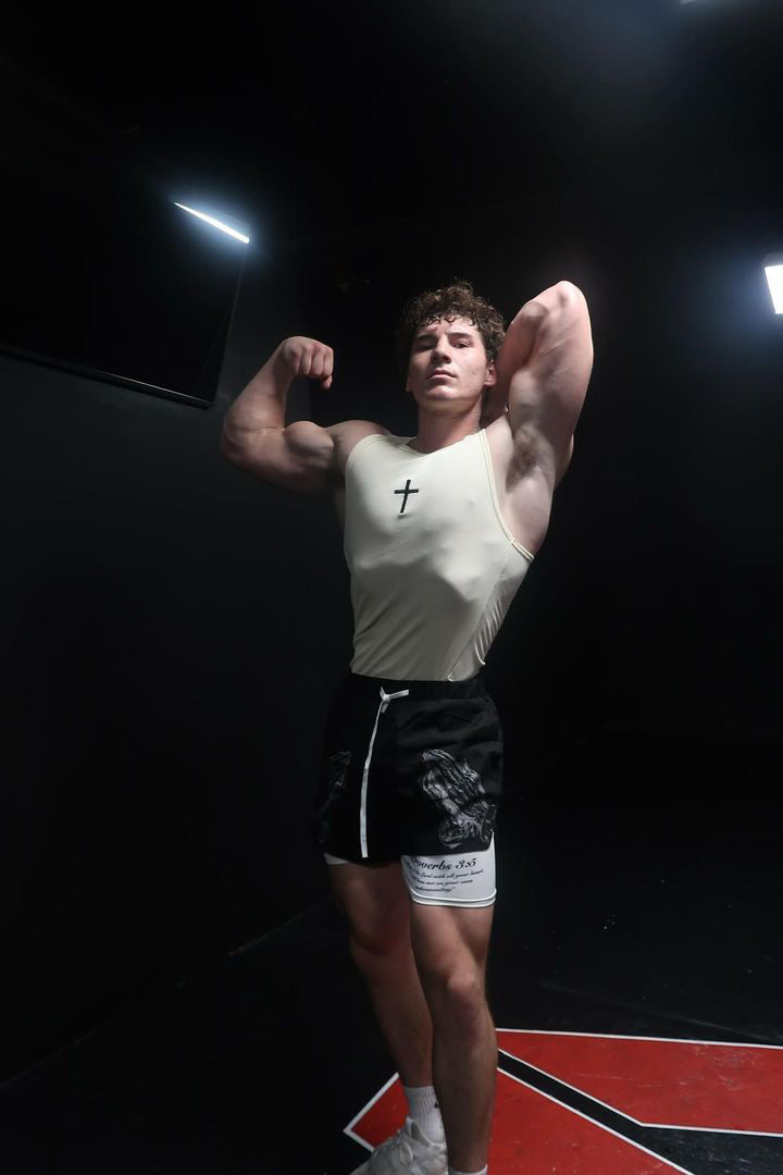 Saint Kaizen Cross Stringer - Cream. Christian gym wear tank top with a bold cross symbol design. Deep-cut, performance fit for maximum range of motion during lifts.